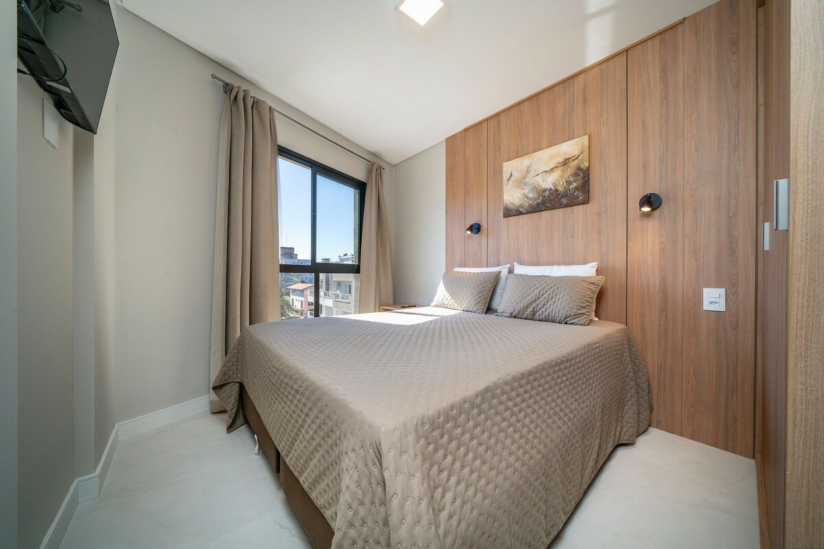 A bedroom with a large bed, a window with curtains, a wooden wall panel, and a painting.
