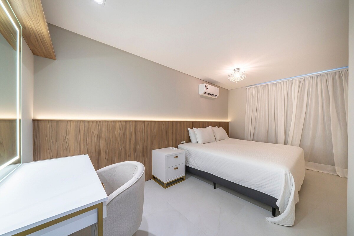 Un dormitorio moderno con cama, mesita de noche y pequeña mesilla.