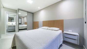 Quarto moderno com cama grande, mesas de cabeceira, espelho e cabeceira de madeira.