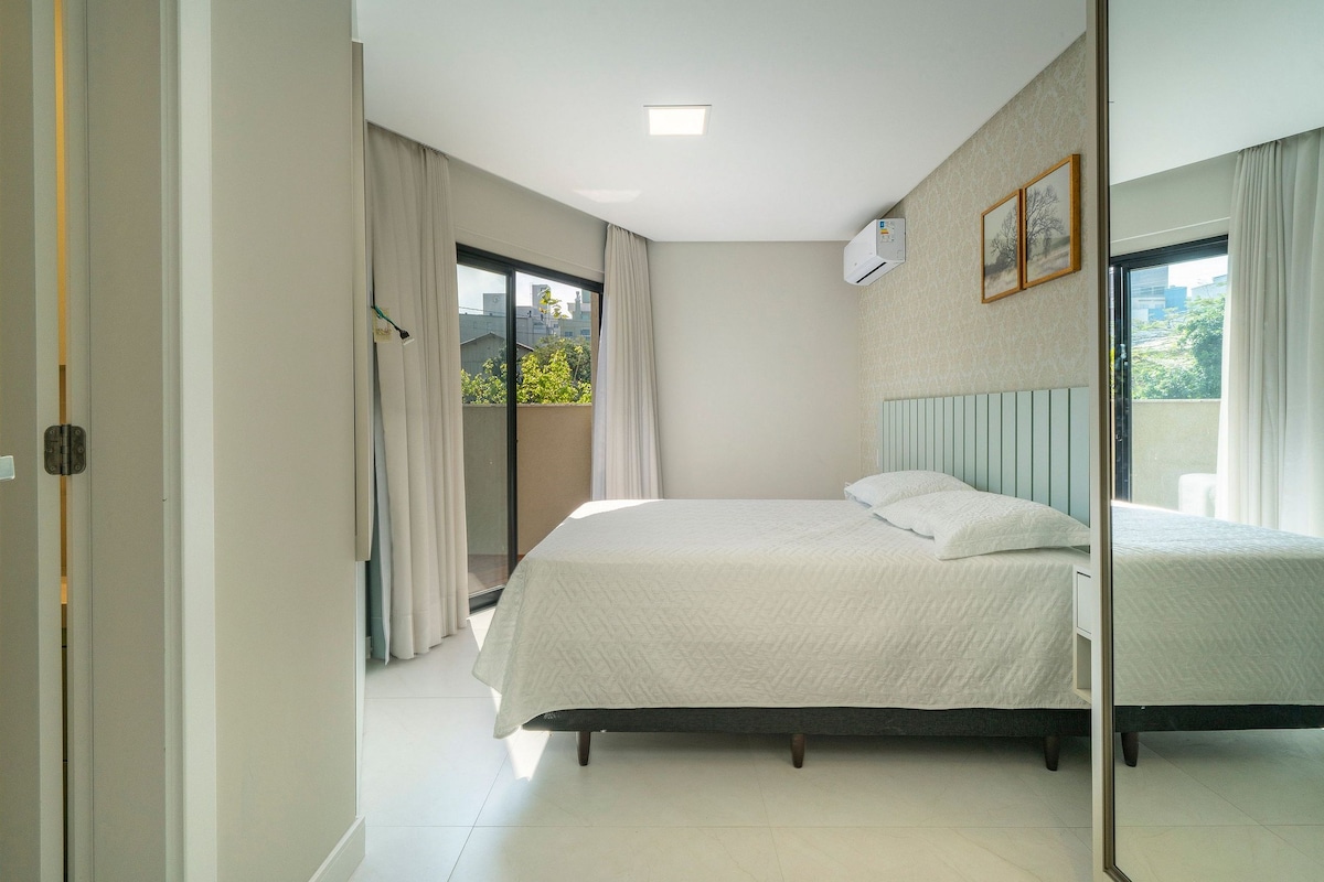 Un dormitorio con cama, ventana con cortinas, equipo de aire acondicionado y vista a zonas verdes.