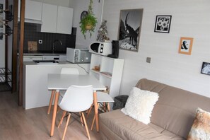 A compact kitchen with white cabinets, a dining table with chairs, and a sofa with a fluffy pillow.