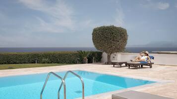 A swimming pool with a clear view of the sea and mountains in the background.