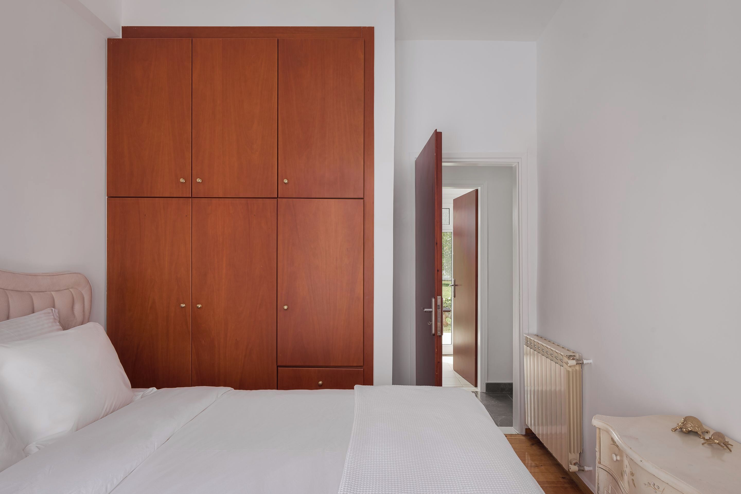 A bedroom with a large wooden wardrobe, a bed with white bedding, and a radiator.