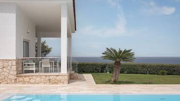 A poolside area with a view of the sea, a stone wall, and a palm tree.