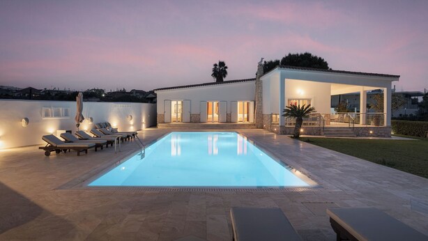 Una casa moderna con piscina, sillones de descanso y un patio cubierto.