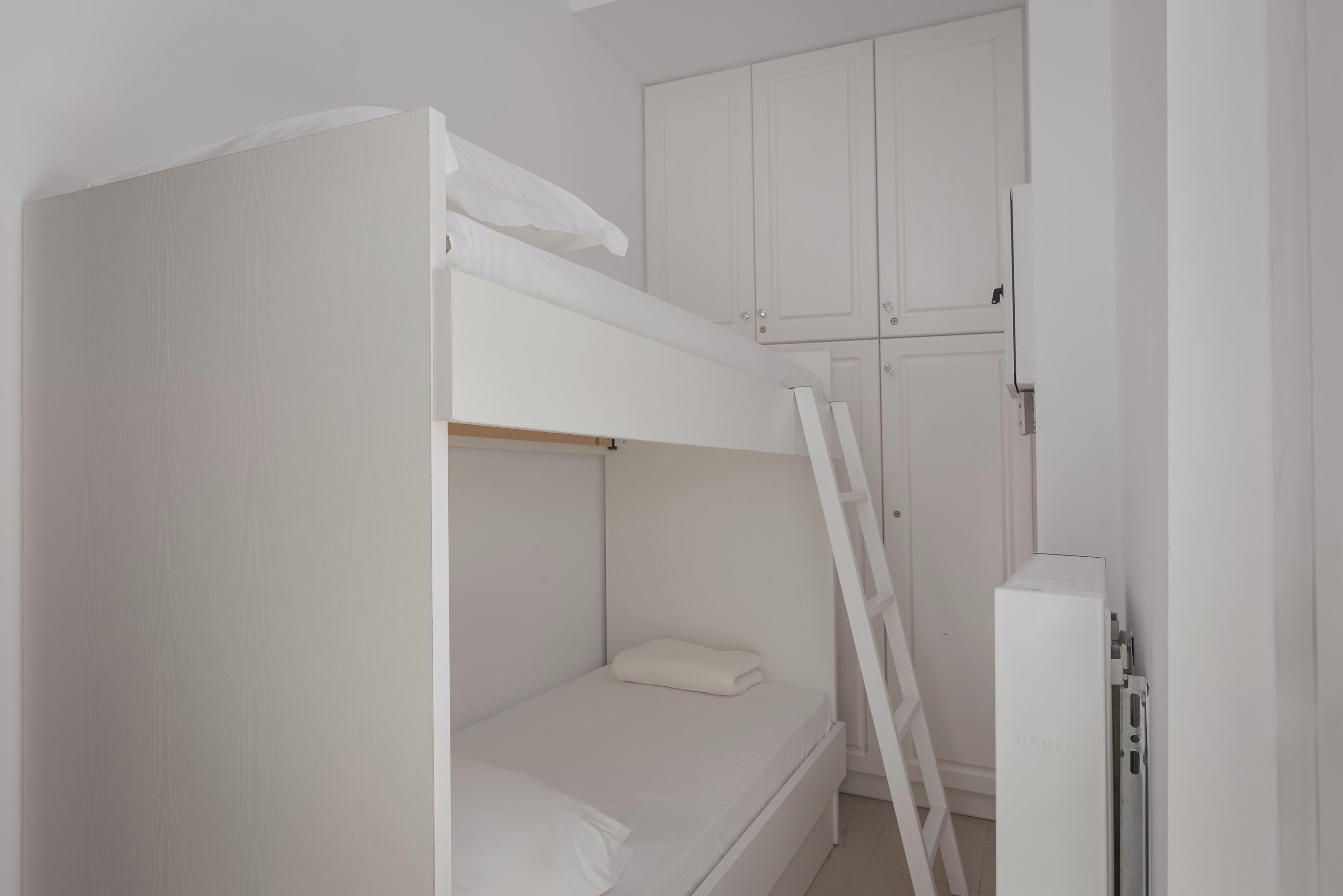 A bunk bed with a ladder, white walls, and a cabinet.