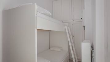 A bunk bed with a ladder, white walls, and a cabinet.