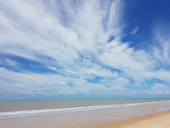 A beach with a wide sandy shore and a clear sky with scattered clouds.
