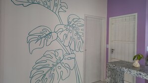 Une pièce avec une grande fresque murale représentant une plante, une porte blanche et un comptoir en marbre sur lequel est posé un petit vase.