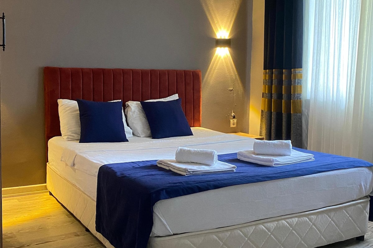 Habitació d'hotel amb un llit gran, un capçal vermell i una làmpada de paret.