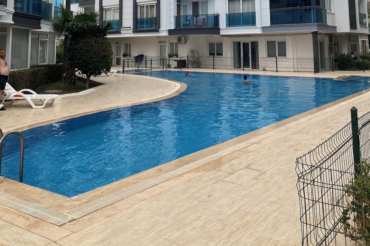 Edifici d'apartaments modern amb piscina, balcons i un cel serè.