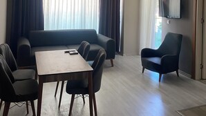Ein modernes Wohnzimmer mit einer Couch, einem Esstisch und Stühlen. Es gibt einen Deckenventilator, eine Klimaanlage und einen an der Wand montierten Fernseher.