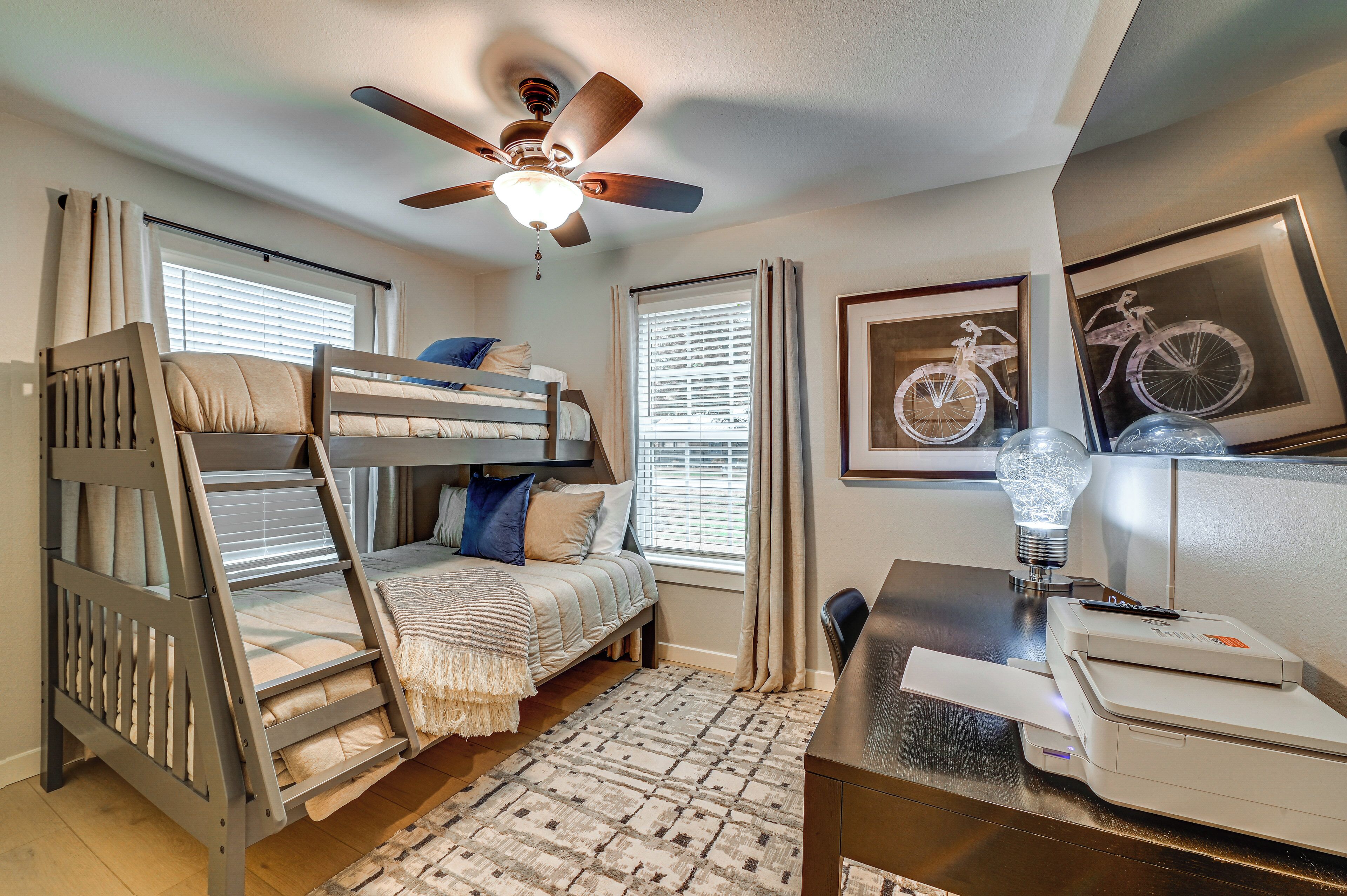 A bunk bed room with a ceiling fan, a desk with a printer, and framed bicycle artwork on the wall.
