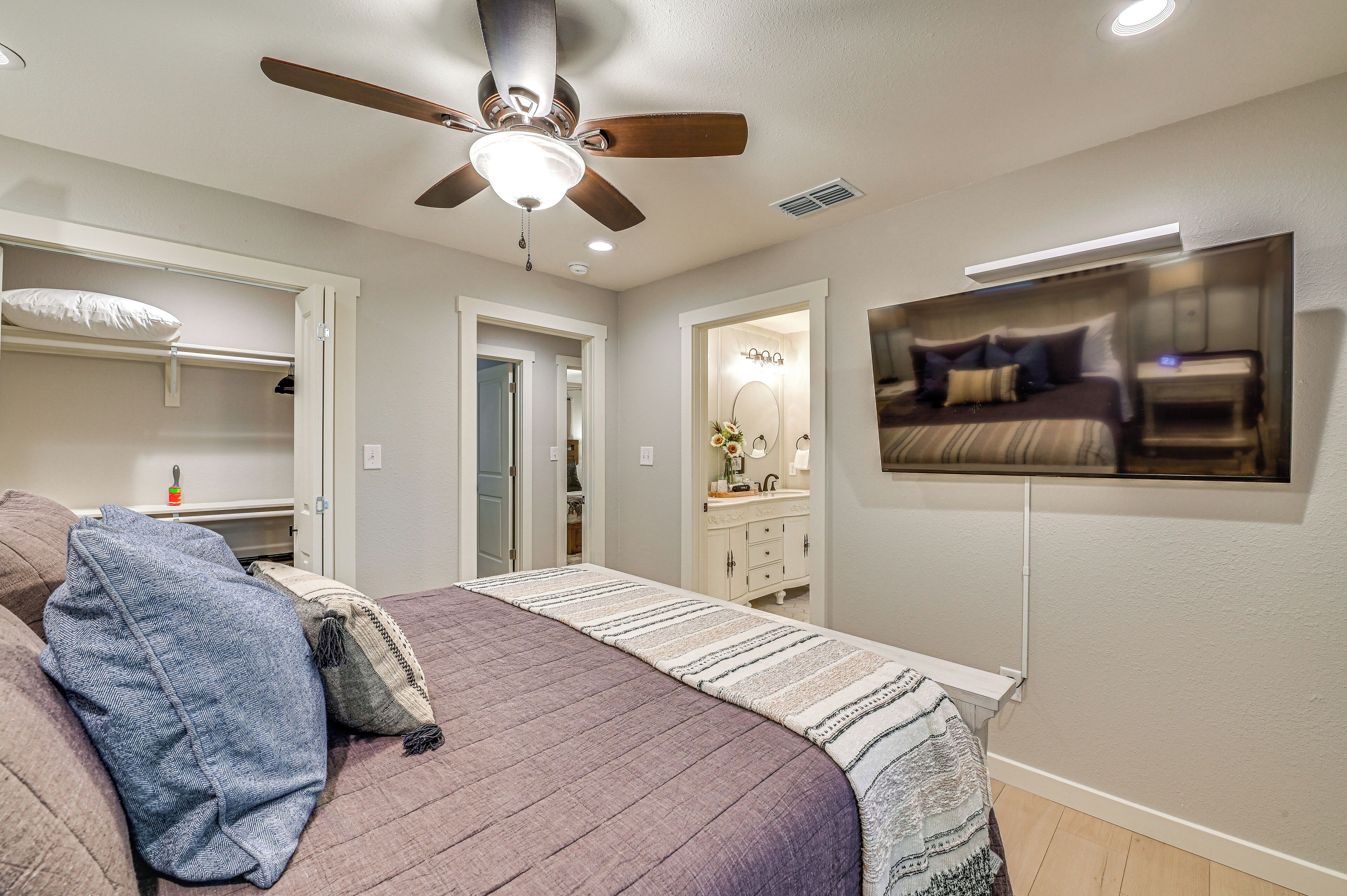 A bedroom with a bed, a ceiling fan, a TV mounted on the wall, and a walk-in closet.