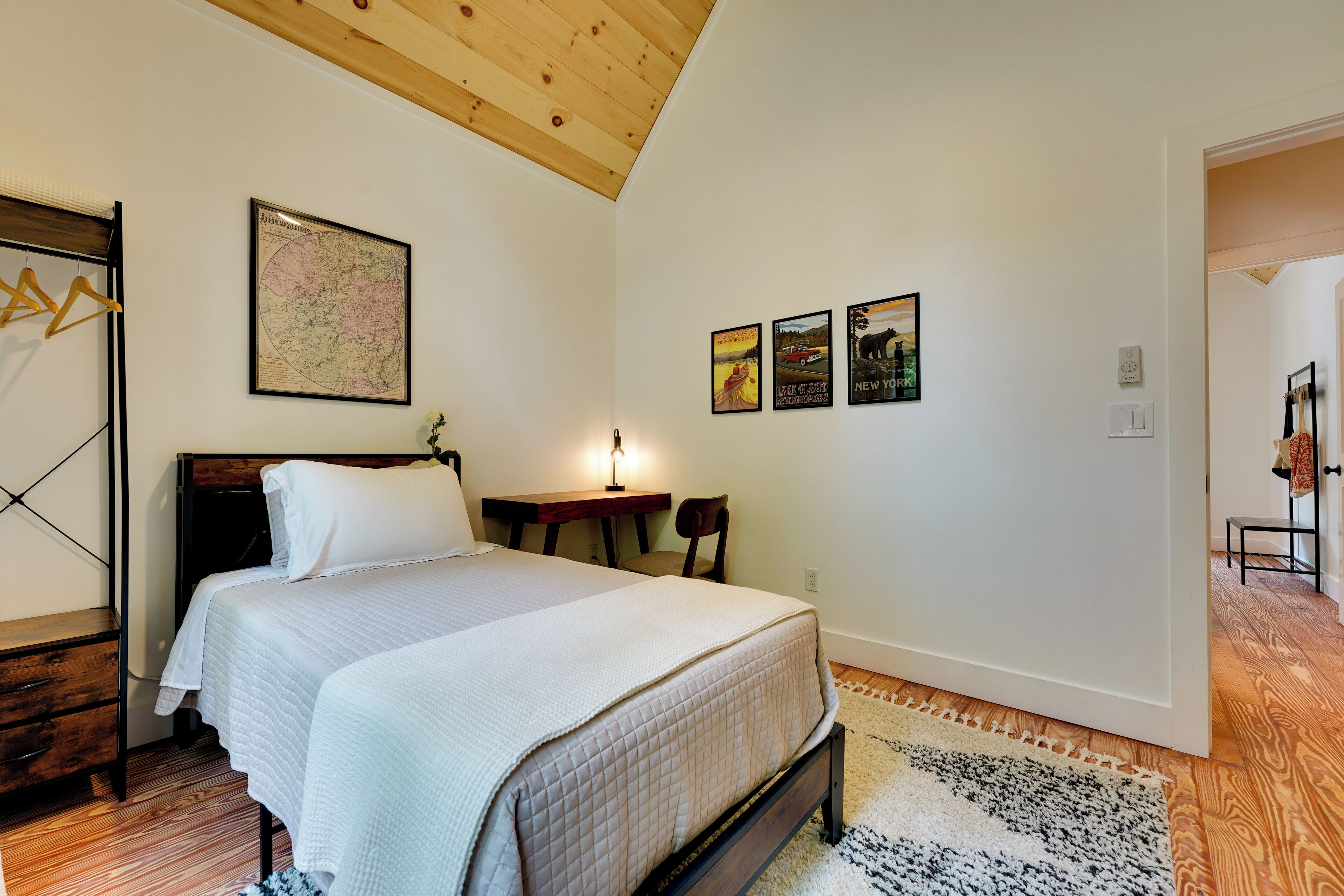 A bedroom with a bed, a desk, and a chair. There is a map on the wall and a poster.