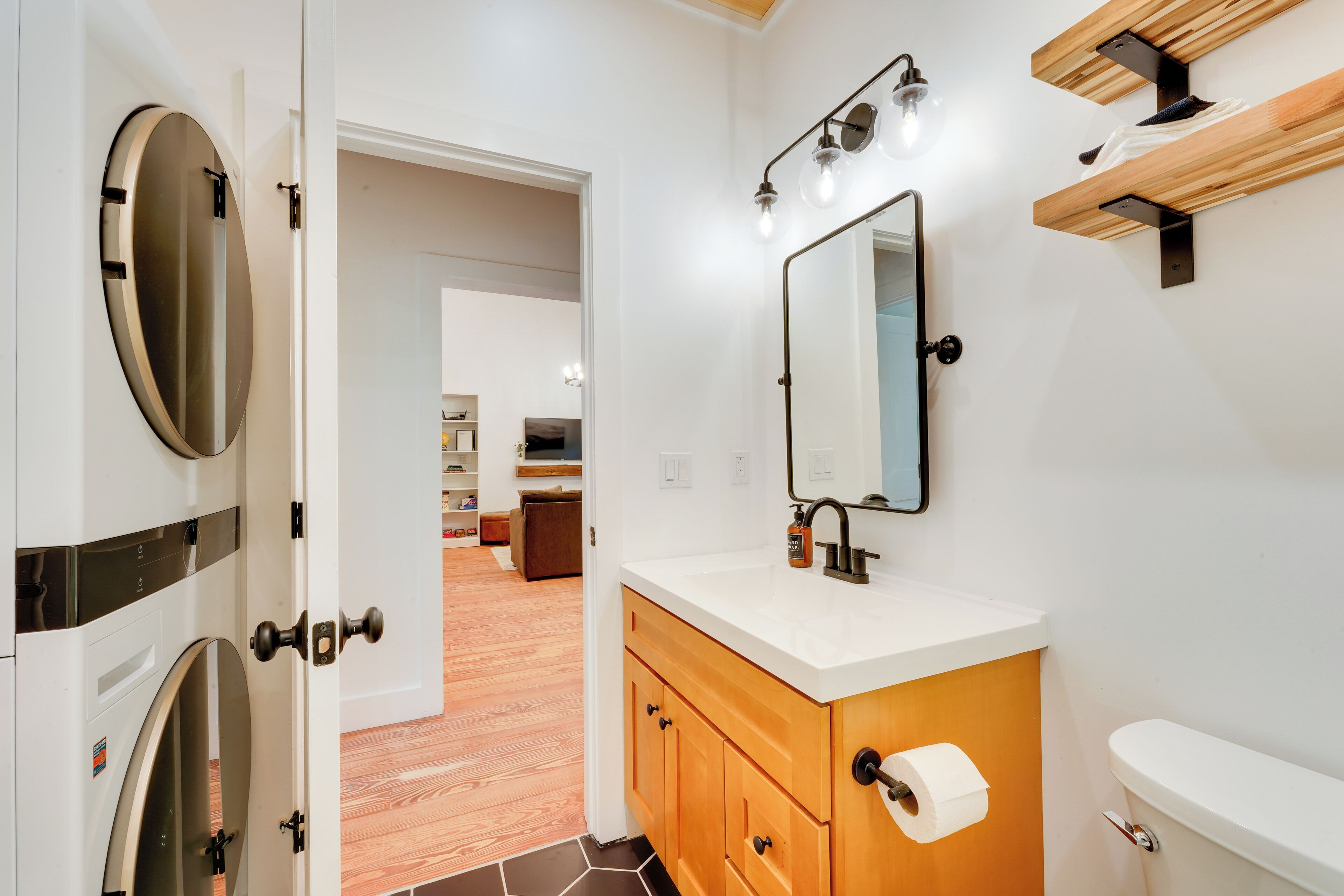 A modern bathroom with a toilet, sink, and mirror. There is a wooden cabinet under the sink and a towel rack above it.