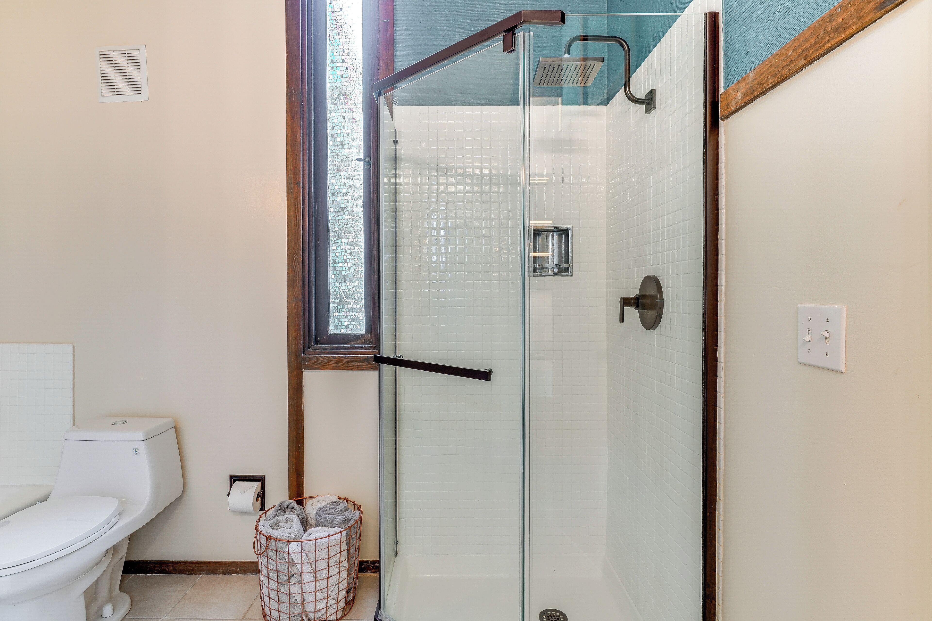 Un baño con ducha de vidrio, inodoro y ventana.