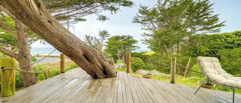 Una terraza de madera con una tumbona, rodeada de árboles y vistas al mar.