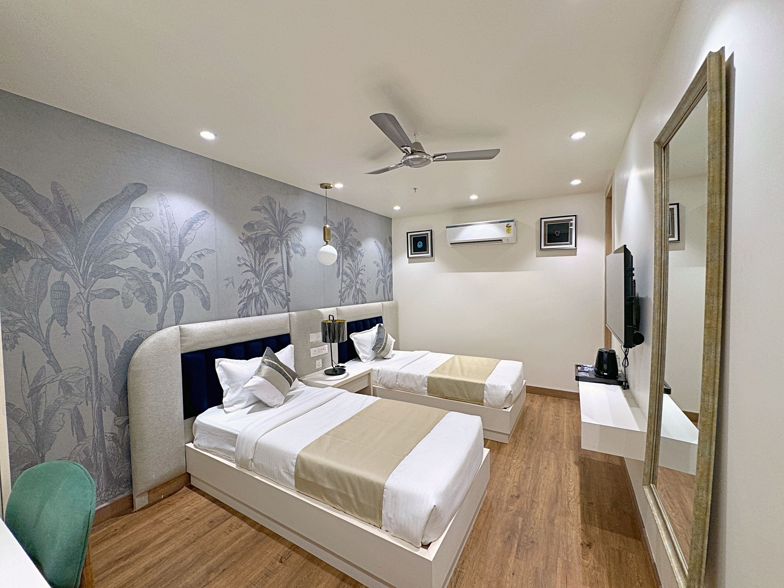 A hotel room with two beds, a ceiling fan, an air conditioning unit, a television, and a mirror.