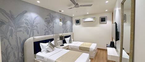 A hotel room with two beds, a ceiling fan, an air conditioning unit, a television, and a mirror.