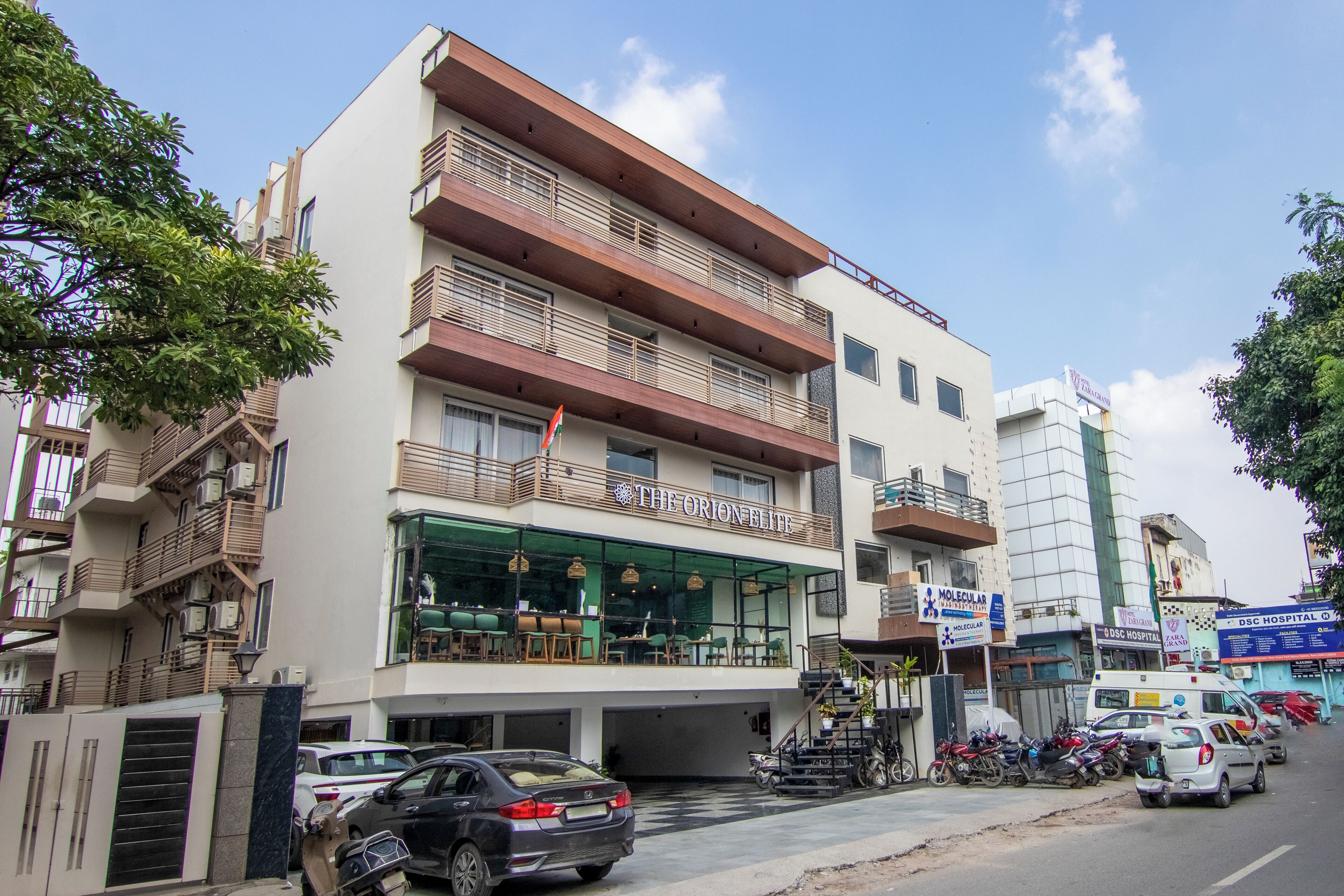 A multi-story building with a restaurant on the ground floor, balconies, and a parking area with cars and motorcycles.