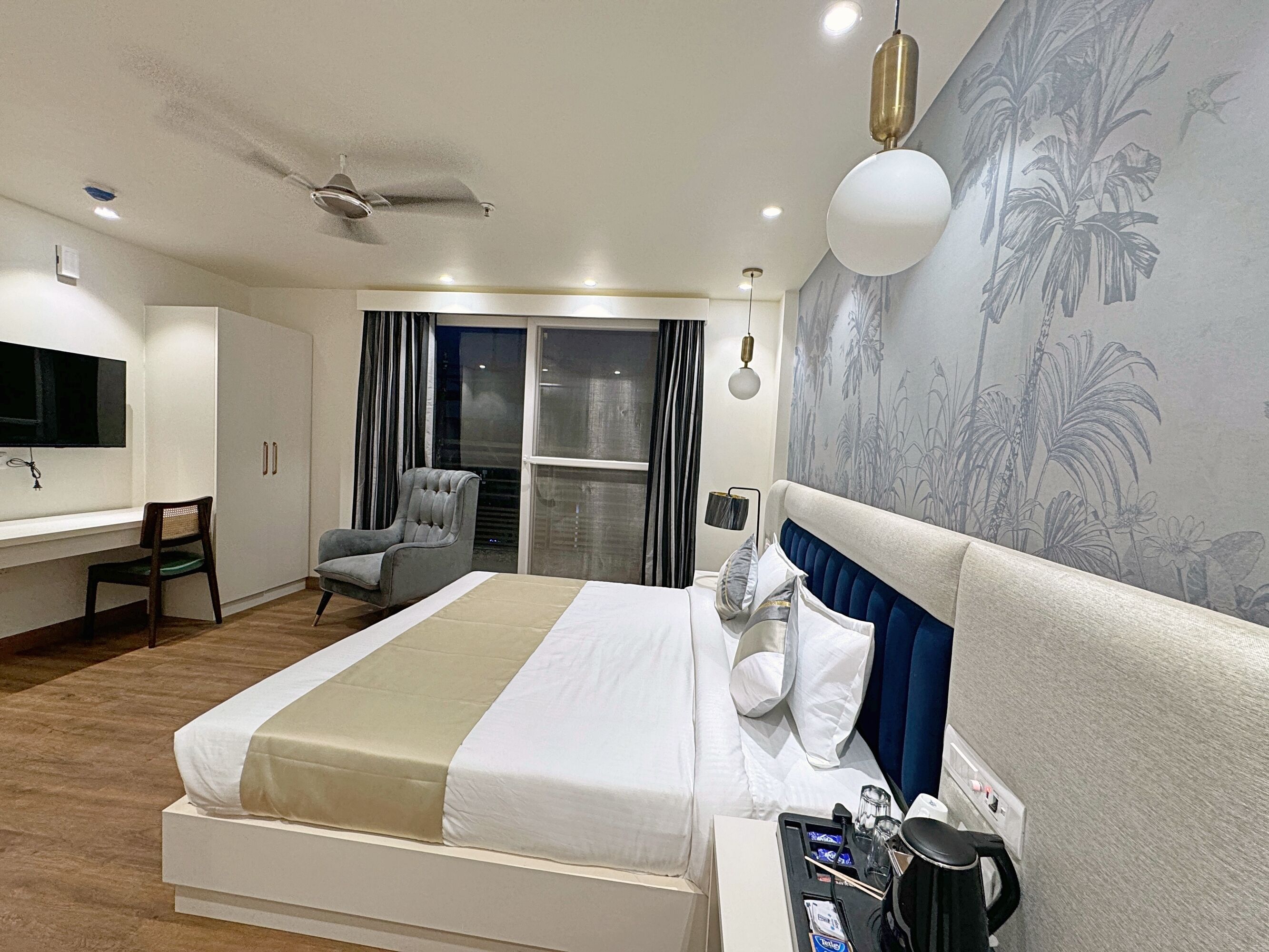 Ein modernes Hotelzimmer mit einem großen Bett, einem Schreibtisch, einem Sessel, einem Fernseher und einem Deckenventilator.