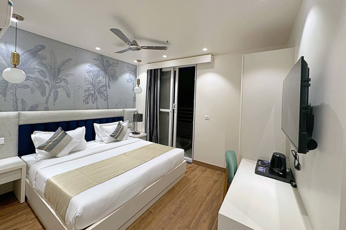 Ein modernes Hotelzimmer mit einem großen Bett, einem Schreibtisch mit Flachbildfernseher, einem Deckenventilator und einer Schiebetür zum Balkon.
