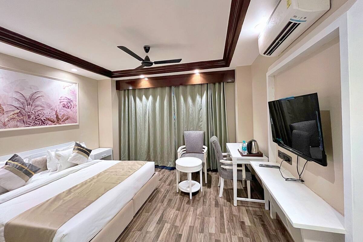 Ein Hotelzimmer mit Bett, Schreibtisch mit Stuhl, Fernseher und Deckenventilator.