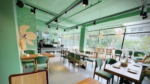 A modern cafe with green walls, wooden tables, and chairs. - The Orion Elite (New Delhi)