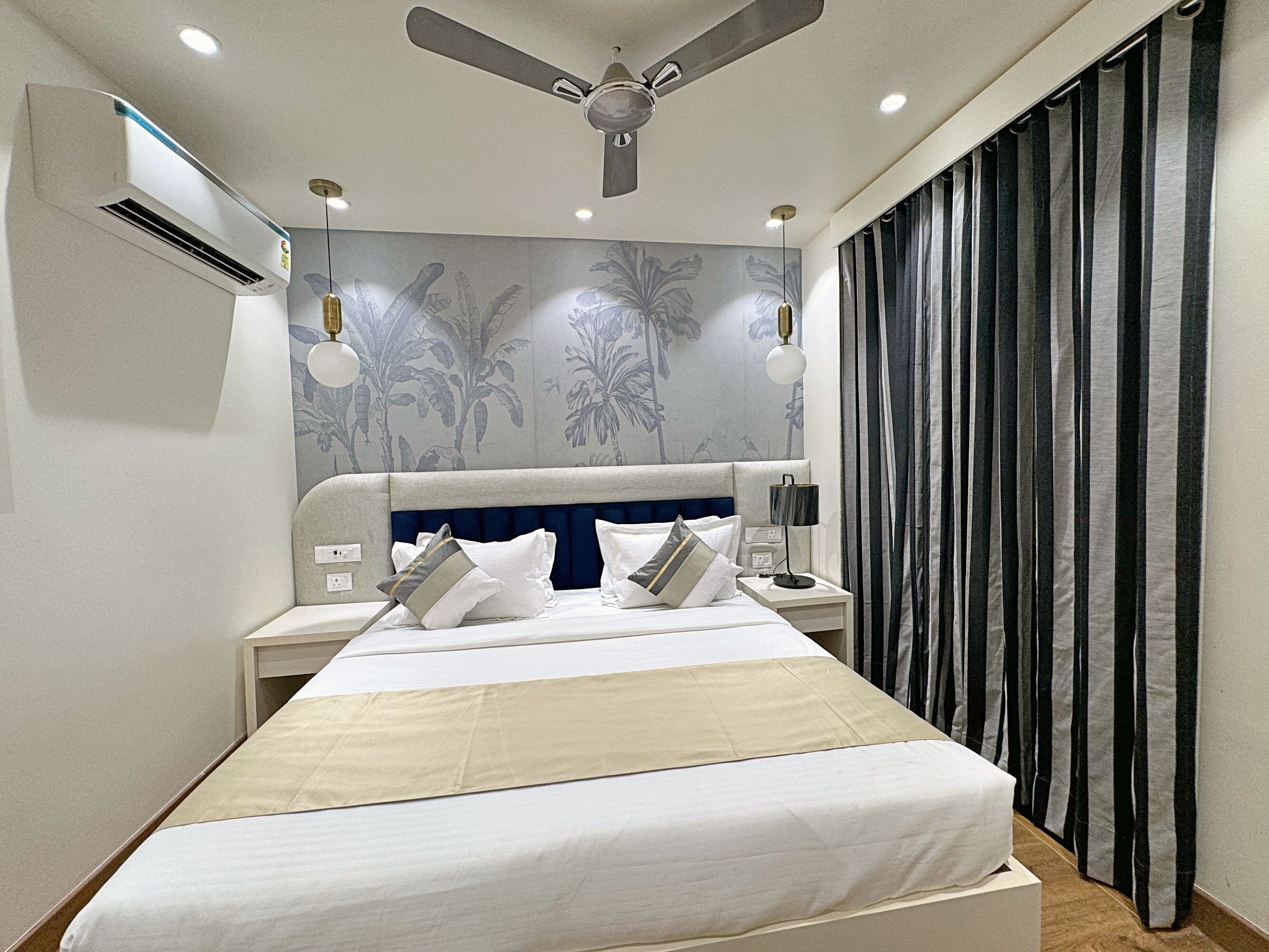 A modern hotel room with a bed, nightstands, a ceiling fan, and a large window with curtains.