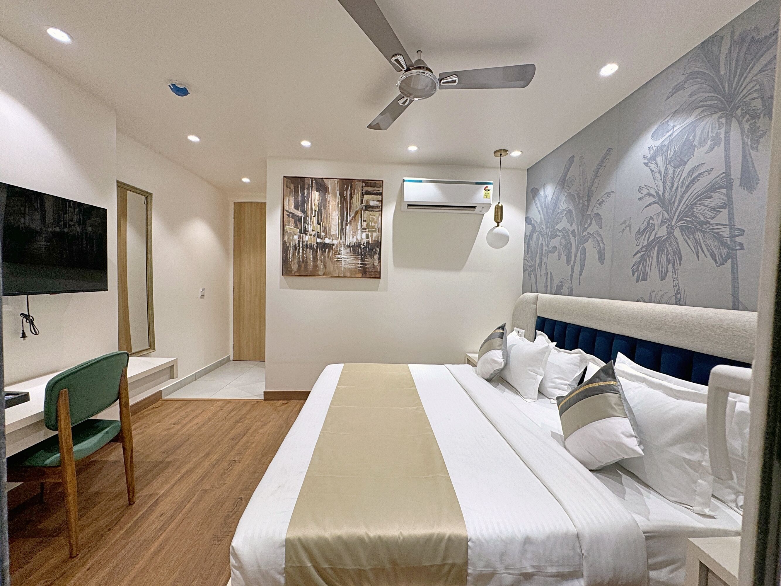Habitación de hotel con cama, escritorio, silla, ventilador de techo y televisor montado en la pared.
