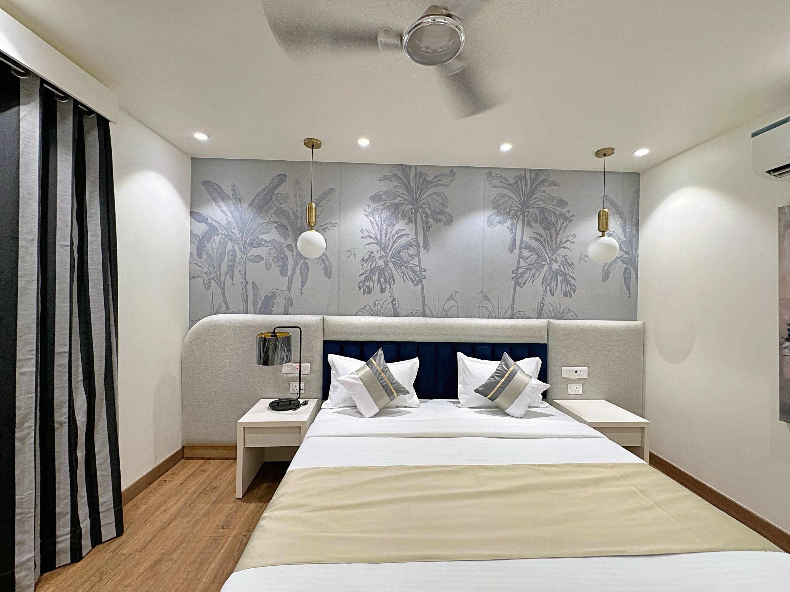 A modern hotel room with a large bed, two bedside tables, a ceiling fan, and a wall with a tropical wallpaper design.