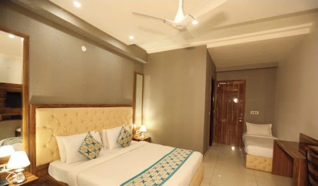 A hotel room with a large bed, a desk, a chair, a mirror, and a ceiling fan.