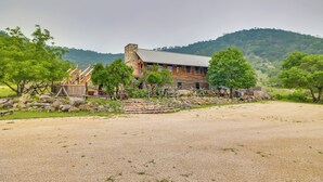 A rustic cabin with a stone chimney, surrounded by a gravel driveway and a fenced area. - Rural Texas Villa w/ Hot Tub - Horses Welcome! (Tarpley)