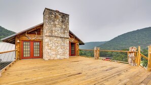 A wooden deck with a stone chimney, red doors, and a view of a mountain. - Rural Texas Villa w/ Hot Tub - Horses Welcome! (Tarpley)