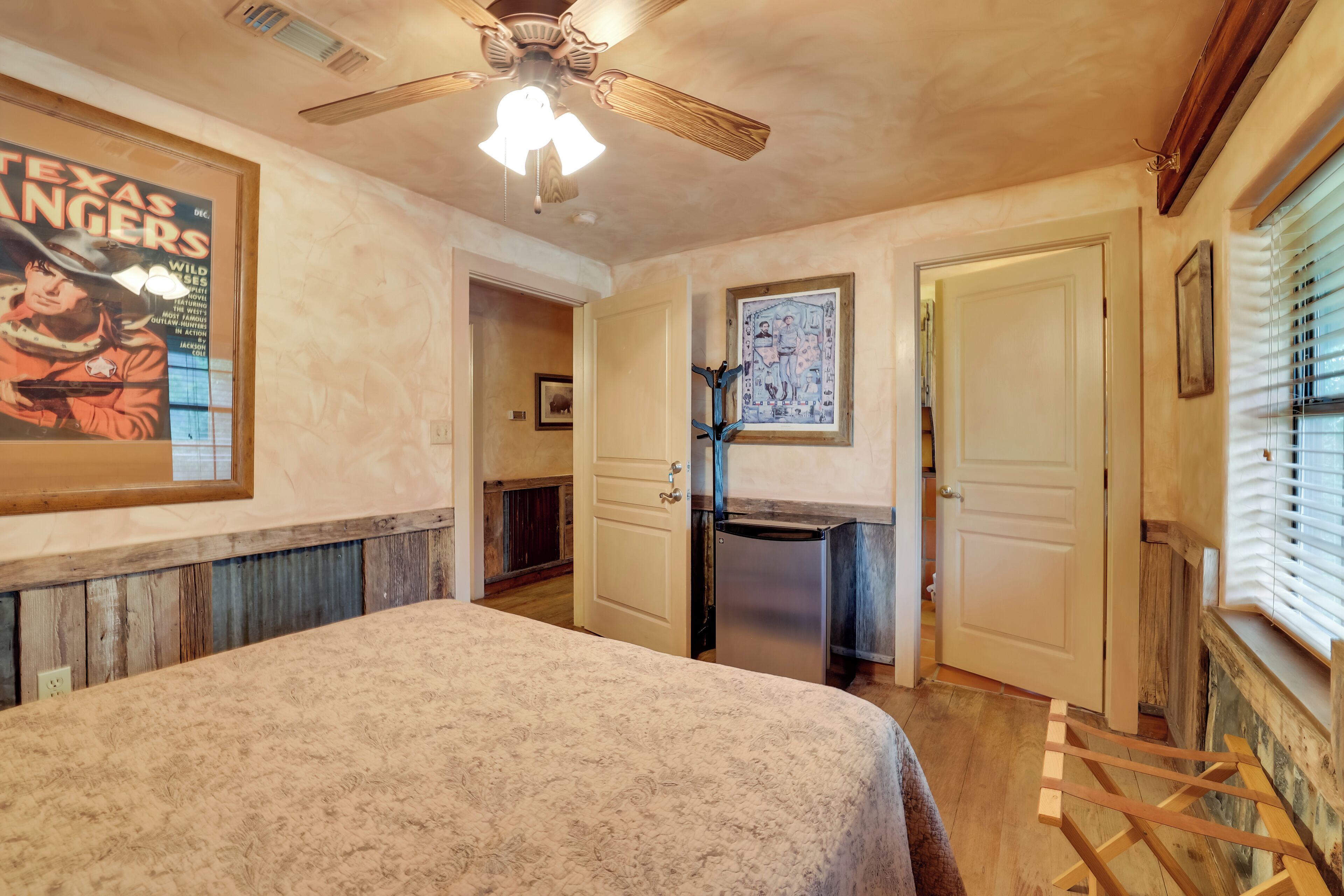 A bedroom with a bed, a ceiling fan, a wooden desk, and a window with blinds.