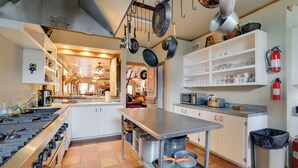 A kitchen with a gas stove, hanging pots, a microwave, and shelves with kitchenware. - Rural Texas Villa w/ Hot Tub - Horses Welcome! (Tarpley)