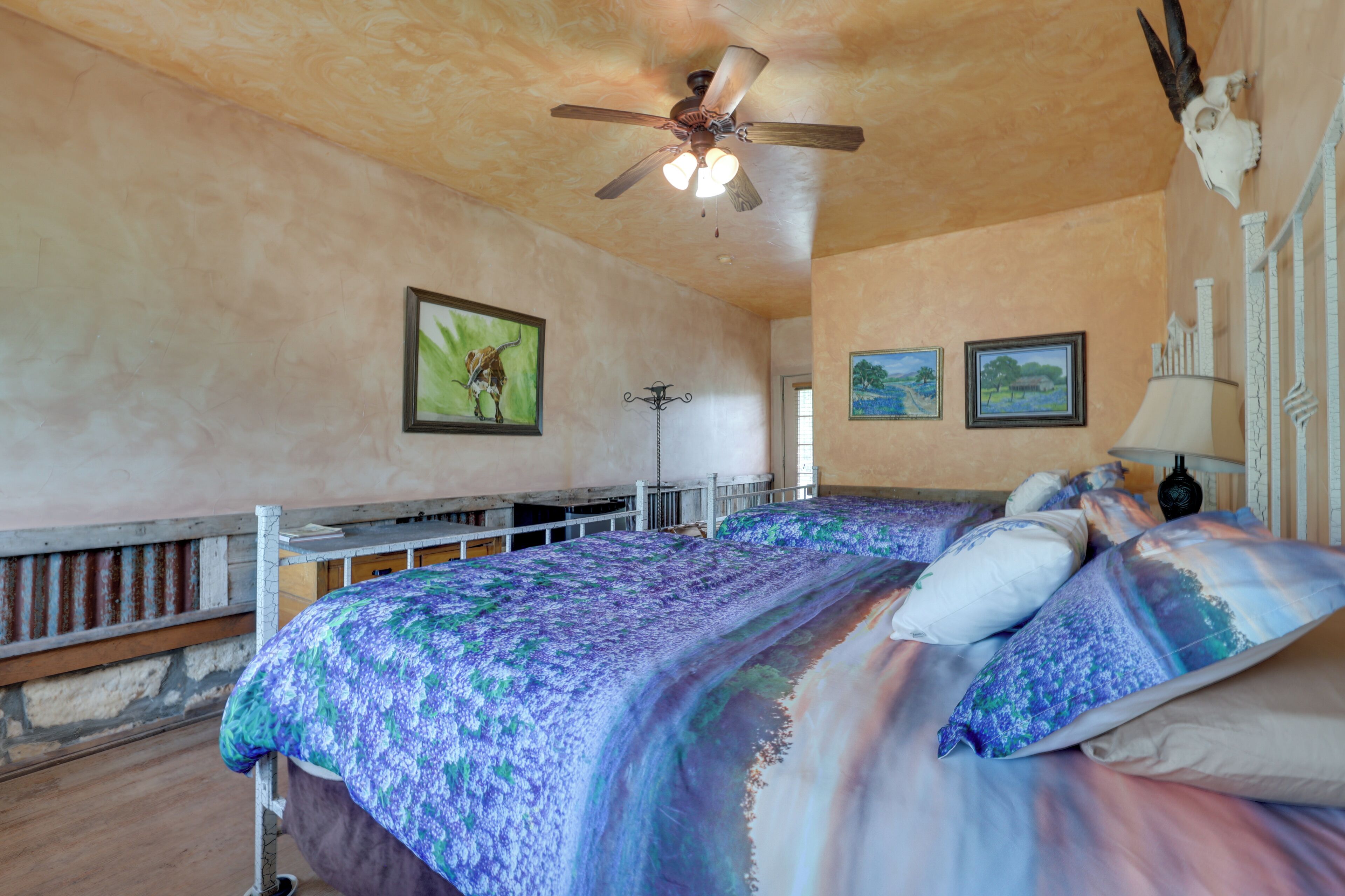 A bedroom with a bed, ceiling fan, and artwork on the walls.