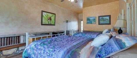 A bedroom with a bed, ceiling fan, and artwork on the walls.
