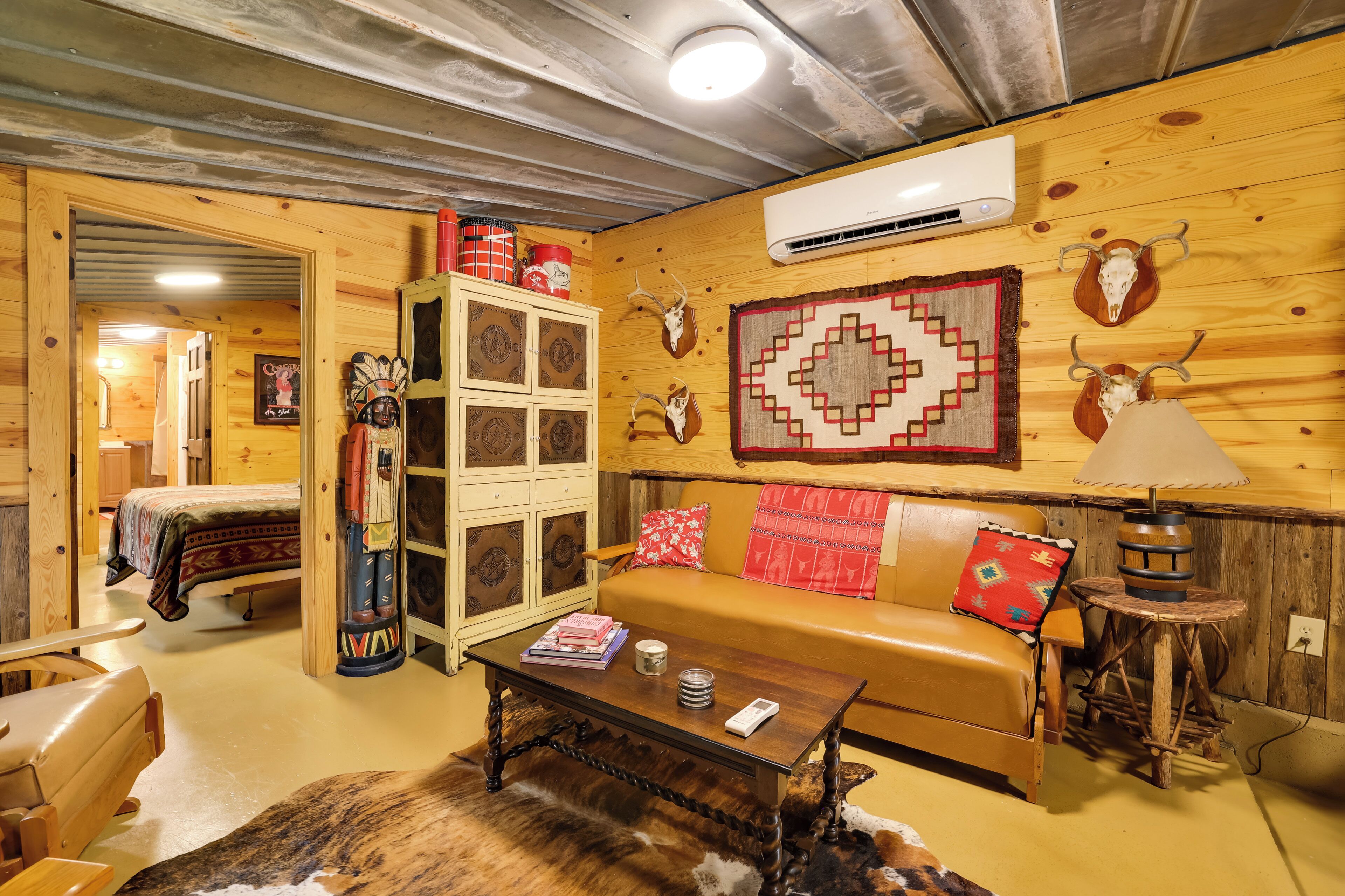 A cozy room with a wooden ceiling, a sofa with red cushions, a coffee table, and a lamp.