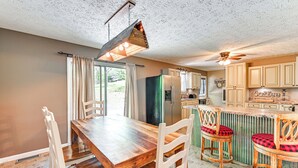 Une cuisine avec une table à manger en bois, des chaises blanches, un luminaire suspendu et un ventilateur de plafond.