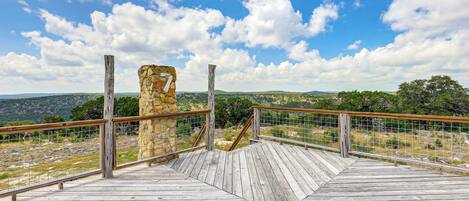 A wooden observation deck with a stone structure in the background, overlooking a hilly landscape.