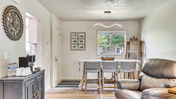 A dining area with a table and chairs, a leather sofa, a decorative wall clock, and a window with a view of trees. - Cozy Meyers Lake Townhome: Near Hall of Fame! (Canton)