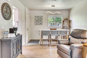 Un coin repas avec une table et des chaises, un canapé en cuir, une horloge murale décorative et une fenêtre donnant sur les arbres.