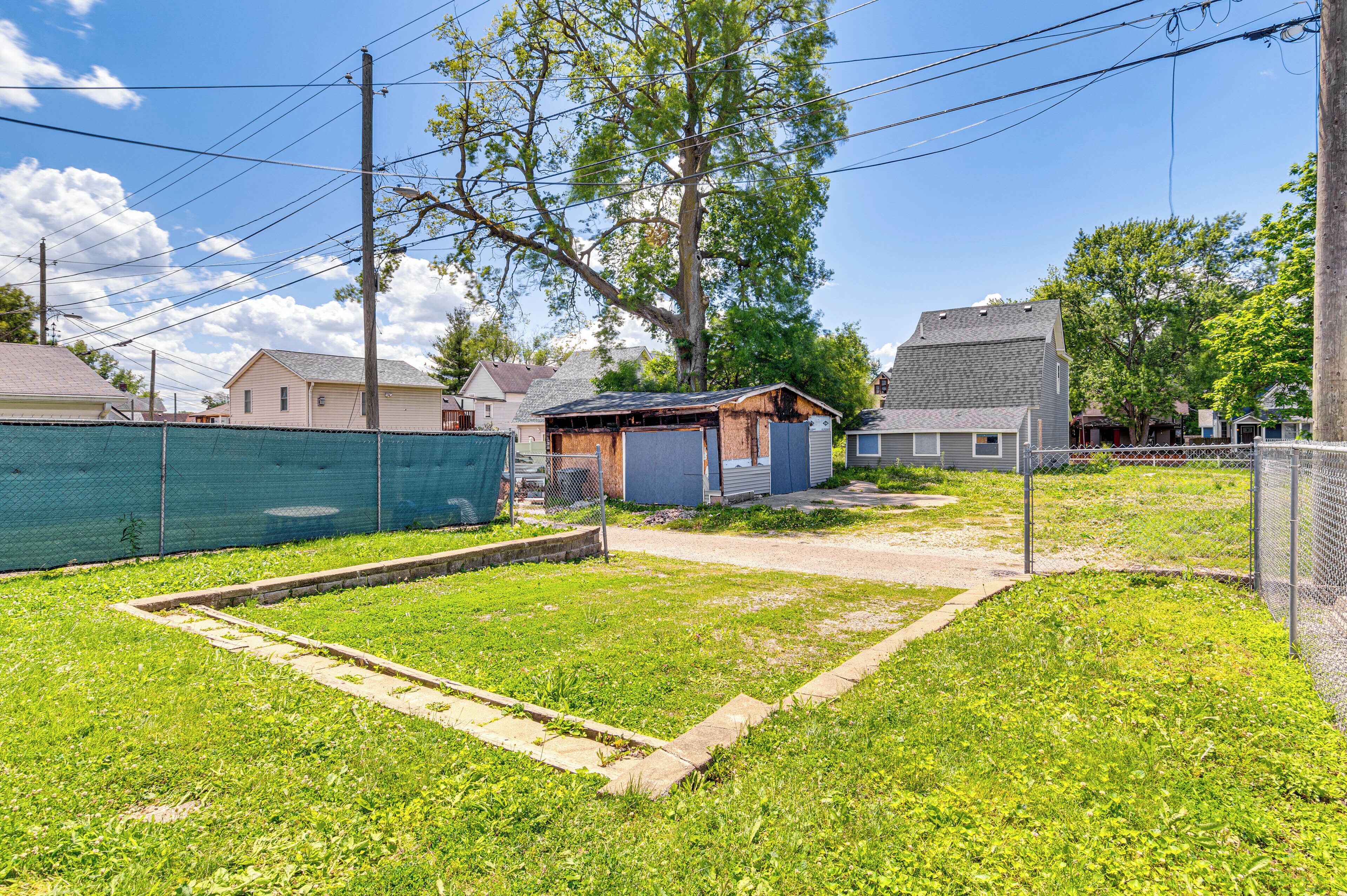 A fenced yard with a small shed, a grassy area, and houses in the background.
