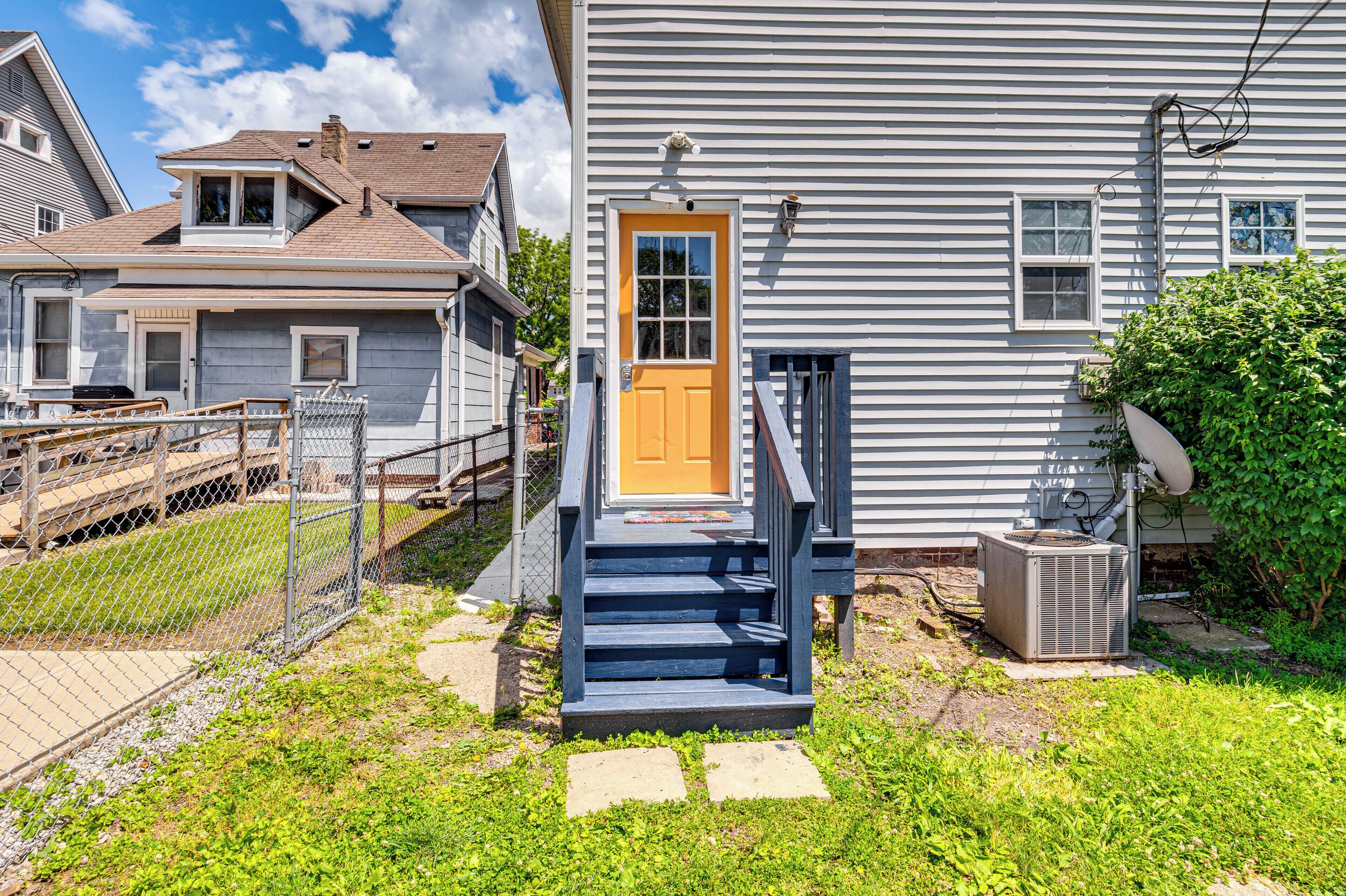 A residential house with a front porch, a yellow door, and a small set of stairs leading to the entrance.