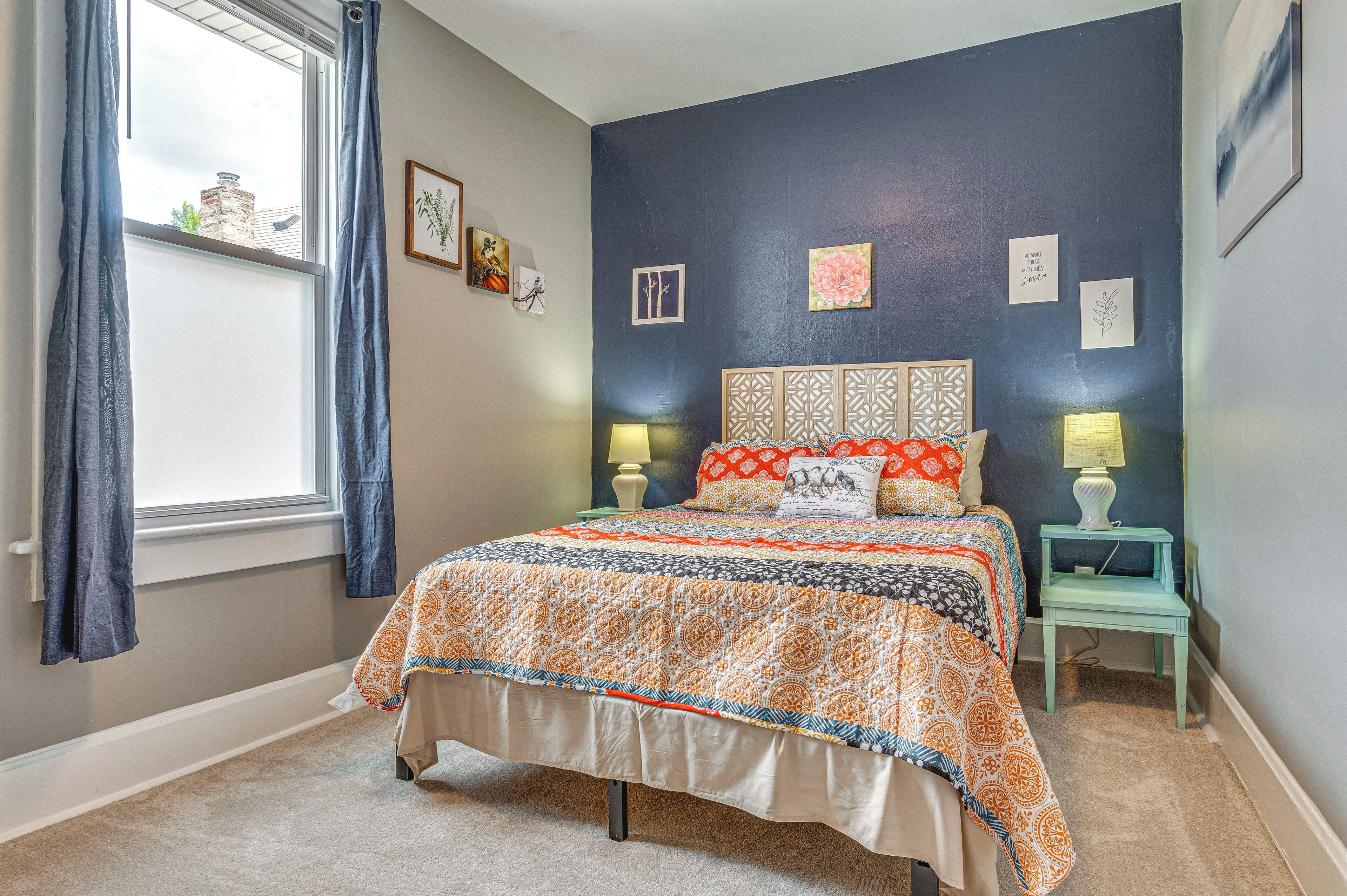 A bedroom with a bed, two bedside tables, a window with curtains, and wall decorations.