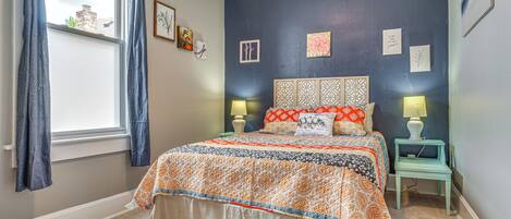 A bedroom with a bed, two bedside tables, a window with curtains, and wall decorations.