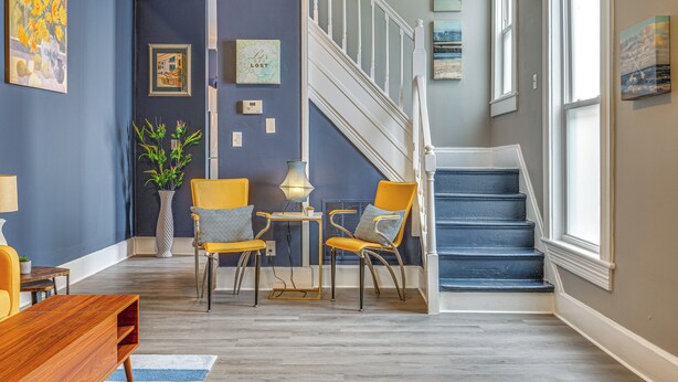 Ein modernes Wohnzimmer mit Treppe, das eine blaue Wand, Holzdielen und eine Mischung aus moderner und klassischer Möbel besticht.