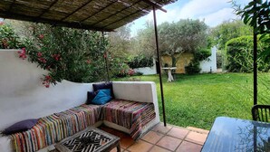 Eine überdachte Terrasse mit einer gepolsterten Sitzecke, einem kleinen Tisch und Blick auf einen gepflegten Garten.